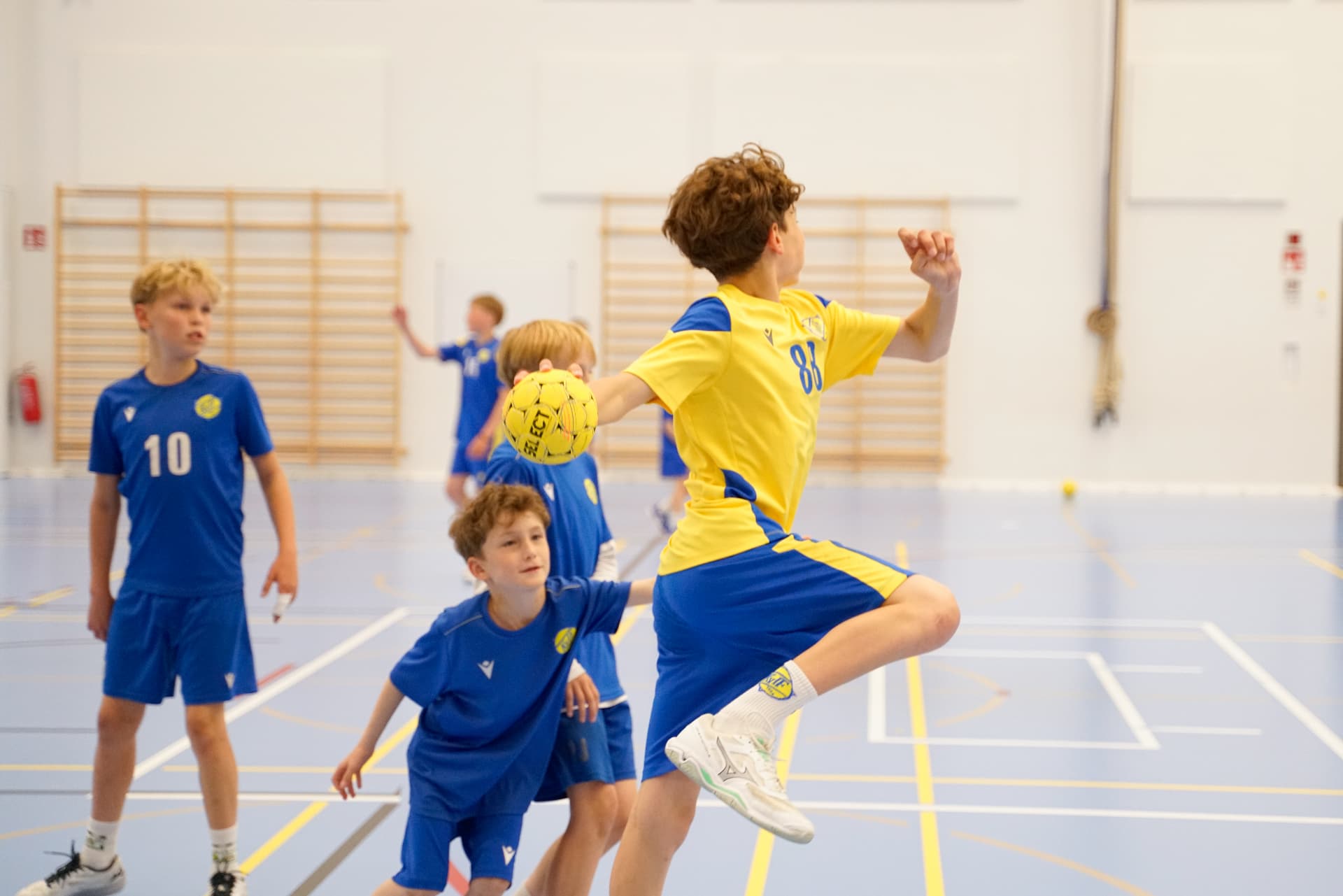 KyIF-spelare i gult gör hoppskott i hallen medan motståndare i blått försvarar